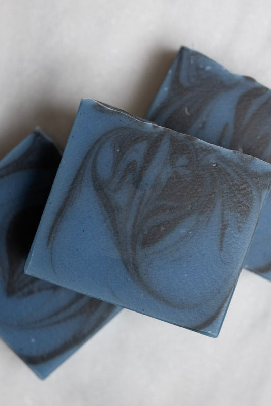 A close-up image of bars of Moose Hunt cold process soap with a blue color and swirled with black pattern.